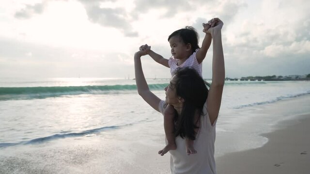 mother carrying her daughter on shoulders at the beach