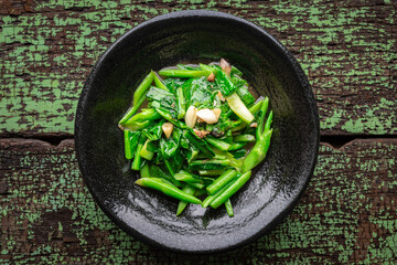 stir fried collards with salted fish and garlic in black ceramic plate on green old wood texture...