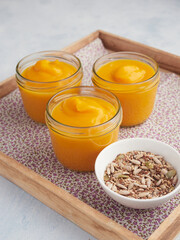 Tray with three individual portions of pumpkin and carrot soup in glass jars, next to seeds for seasoning. Portion size control food concept