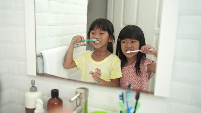 two asian little girl brushes her teeth with sibling together
