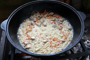 Details of cooking pilaf in cauldron on fire
