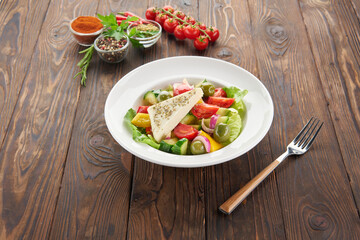 Fresh Greek salad with feta cheese, tomatoes, cucumber, pepper, olives, red onion and lettuce on wooden table, top view. Healthy food, vegetarian dieting, cooking at home concept