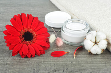 Obraz na płótnie Canvas Face cream jar on wooden background with red gerbera, soft face towel and cotton flower.