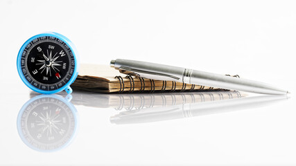 Compass, pen and notepad on a white reflective background. Vacation planning concept, travel or tourist trip