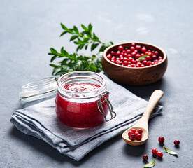 juicy forest lingonberry  in a wooden bowl and handmade jam in jar on gray background. Concept homemade healthy food. Close up