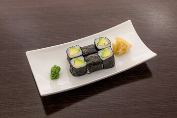 Serving of maki sushi stuffed with ripe avocado, Japanese rice, rolled with nori seaweed, with wasabi and ginseng