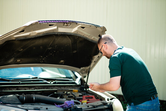 Closeup Portrait, Young Man Having Trouble With His Broken Auto, Opening Hood Trying To Fix Engine, Isolated Green Trees Outside Background. Car Won't Start, Dead Battery