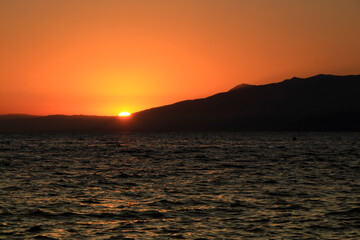 Seascape with mountains and orange sky at sunset