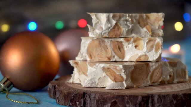 Pieces of nougat with almonds, on a blue background and Christmas decoration, with an unfocused background 