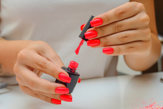 Red nail polish. Hand with red nails on a white background. Close up of female hands with smooth soft skin and bright color manicure pouring nail polish from a bottle. High image quality.
