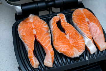 Three raw salmon steaks are toasted on a modern electric non-stick coating grill. Healthy eating concept. Close up photo with selective focus