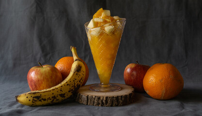 fruit salad in an ice cream cone shaped glass. Surrounded by apples, oranges and bananas.