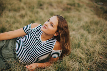 Naklejka na ściany i meble Beautiful young girl lying on the dry grass. Girl in a striped T-shirt and shorts. Portrait of a girl in the woods in nature on a beige background