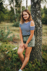 Beautiful young girl lying on the dry grass. Girl in a striped T-shirt and shorts. Portrait of a girl in the woods in nature on a beige background