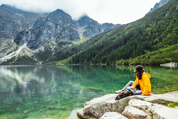 woman backpacker sitting on rock enjoying the view of lake at tatra national park mountains