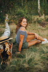 Beautiful young girl sitting on a fallen tree. Girl in a striped T-shirt and shorts. Portrait of a girl in the woods on the nature. Ride a bike in the woods