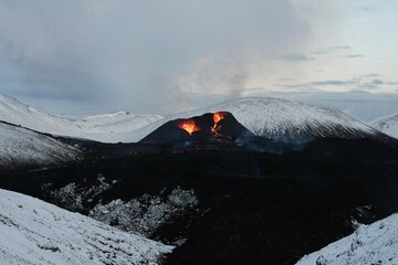 Eruption at Fagradalsfjall volcano, Iceland. Black lava field is framed by a white, snow-covered...