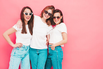 Three young beautiful smiling hipster female in trendy same summer white t-shirt and jeans clothes. Sexy carefree women posing near pink wall in studio. Positive models