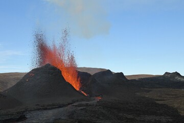 Volcanic vent at Fagradalsfjall, Iceland, erupting incandescent orange and red lava. Black cooled...