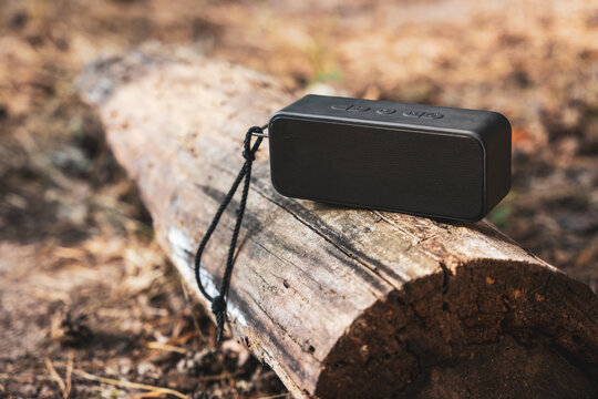 Portable wireless bluetooth speaker for listening to music on a log in the forest