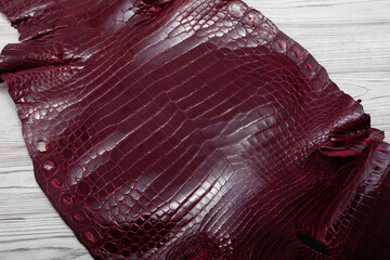 Brown burgundy colored alligator natural leather on the wooden table	
