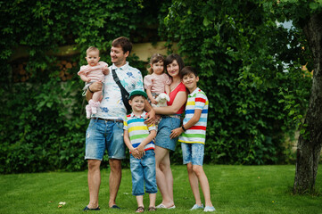 Obraz premium Beautiful large family with young parents and four kids stand in green grass at courtyard.