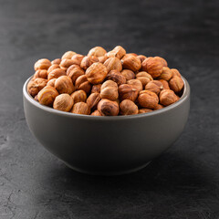Peeled hazelnuts in a bowl on a black textured background, side view. Template for designers or label