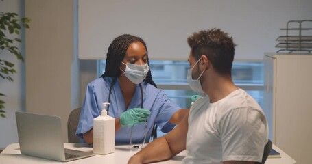 Professional doctor or nurse giving covid-19 vaccine injection to young male patient at clinic.