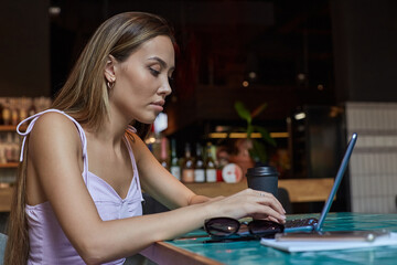 beautiful young asian woman sitting at table of coffee shop, working on laptop. attractive student lady studying at cafe, doing homework. modern online education, distant work, remote job, freelance