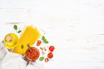 Italian food background on white kitchen table. Pasta, tomato sauce, olive oil and basil. Top view with copy space.