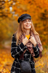 Fototapeta na wymiar Autumn portrait of happy smiling woman with hat and scarf in fashion coat on nature in park with yellow fall leaves