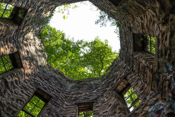 a stone cylinder shaped building in the forest covered with colorful graffiti surrounded by lush...