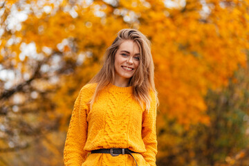 Happy autumn portrait of a beautiful smiling girl in a fashion yellow knitted sweater in nature...