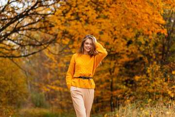 Beautiful happy young caucasian girl with smile in a fashion vintage yellow sweater walks in an autumn park with bright colored foliage
