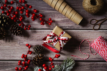 Christmas composition with holiday decoration, present, berries, cones, branches on dark wooden background. Festive holiday greetings. Holiday craft gift wrapping. Merry Christmas.
