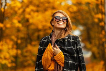 Happy beautiful young smiling woman with cute face in trendy black coat, knitted sweater, scarf and...