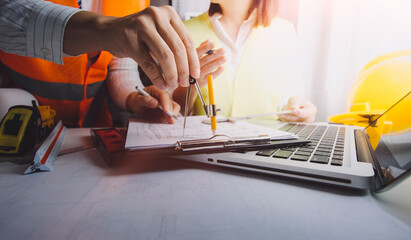 Two colleagues discussing data working and tablet, laptop with on on architectural project at construction site at desk in office