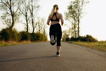 Young sporty girl running on a  road at sunset.   Lifestyle sports motivation. 