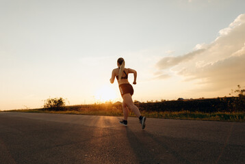 Fototapeta na wymiar Young sporty girl running on a road at sunset. Lifestyle sports motivation. 