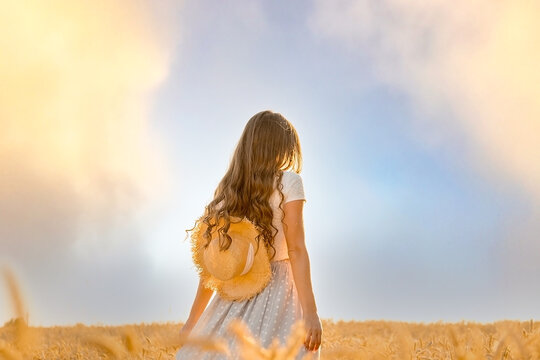 slender beautiful girl dancing in the field, back view. golden ears of wheat on blue sky background, harvest season, crops, horizontal image.