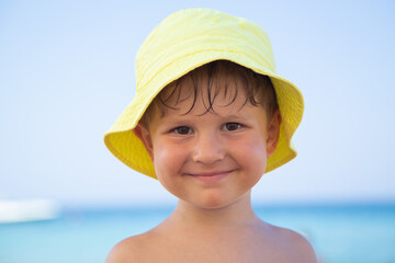 Portrait of a little boy in yellow panama who looks at the camera and smiles. Sea background.