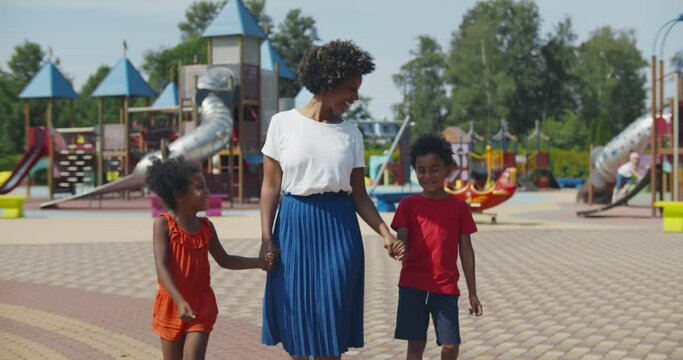 Afro-american mother and two children walking at kids playground
