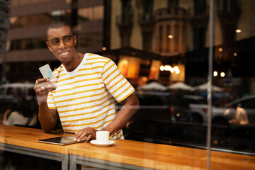 Handsome young african man in cafe drinking coffee. Portrait of happy man with credit card drinking coffee in cafe..
