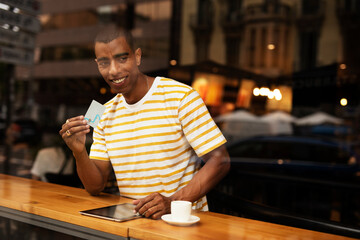 Handsome young african man in cafe drinking coffee. Portrait of happy man with credit card drinking coffee in cafe..