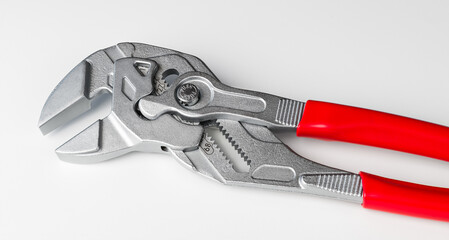 Tongue-and-groove slip-joint pliers detail with movable jaw on white background. Closeup of adjustable wrench with red plastic grips. Hand work tool for holding nuts and bolts, clamping or tightening.