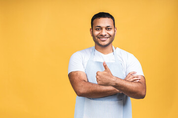 Portrait of positive attractive african american black indian cook man in apron looking at camera isolated over yellow background. Thumbs up.