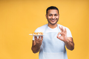 Young african american indian black man eating sushi using chopsticks over isolated yellow background. Cook preparing sushi.