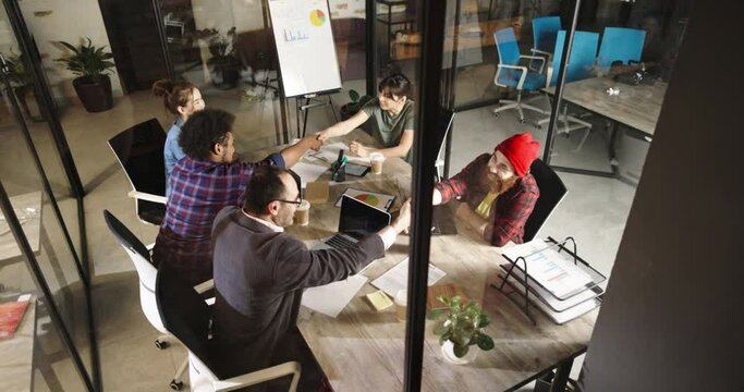 Team of diverse millennial creative businesspeople doing a fistbump while brainstorming on marketing strategy for startup - business success high angle 4k footage