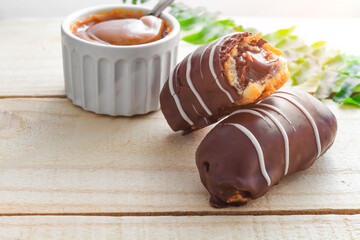 Éclair with Dulce de leche on wooden farm table, spoon on the side and decorated with branch of leaves. Bomba de Chocolate.