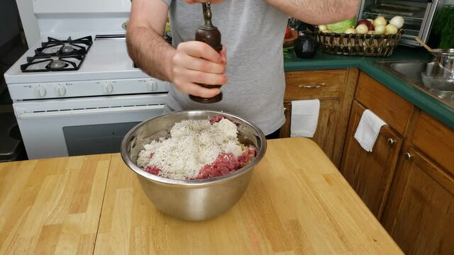 Home cooking - Adding fresh ground pepper and salt into bowl of ground meat with rice and browned onion preparing stuffing for cabbage wraps.